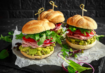 Fresh home sandwich with avocado guacamole, tomatoes, arugula, red onion and ham.