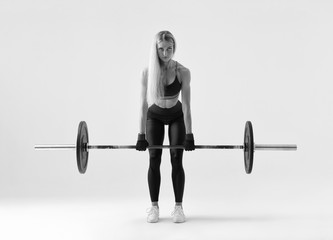 Black and white Front view of confident young blonde woman doing weight lifting workout Attractive young woman bodybuilder lifting barbells looking forward Strong trained body shape arms chest legs