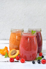 Orange, red and purple smoothies of fresh ingredients - bananas, apricots, raspberries and blueberries on a light background. Healthy food concept. Vegetarian product. Organic Raw Drink. Copy space.