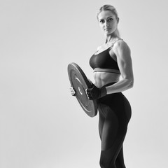 Cropped shot of muscular young female bodybuilder posing with barbell plate on white background...