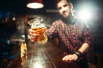 Man holds glass of beer, guy at the bar counter.