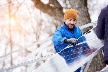 Handsome bearded mature male electrician worker smiling while installing solar pannels on power plant factory copyspace occupation working professionalism confidence job profession environment energy.