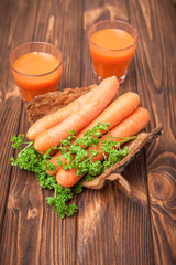 Carrot juice in beautiful glasses, cut orange vegetables and green parsley on dark brown wooden background. Fresh orange drink. Dark mood. Close up photography. Selective focus. Vertical banner