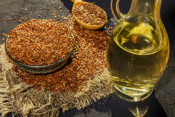 Flax seeds in a clay bowl and linseed oil in a glass jar on a wooden table. Flaxseed oil is rich in...