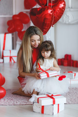 Young beautiful mother and her little daughter,dressed in a beautiful,festive and elegant dress,prepare gifts and red balloons in form of heart for beautiful winter holiday-Valentine's day.