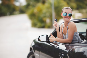 Beautiful young woman in a fancy black convertible.Girl driving a cool car. Cute fun lady,resting one sitting in your car,on a background of green tropical landscape,during summer holidays outdoors