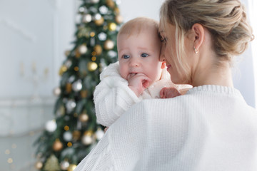 Happy family mother and little son near christmas tree on Christmas Eve at home. A woman and a little boy are resting in the white bedroom near the Christmas tree.  A young mother plays with her son