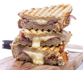 Stack of freshly cooked cheese and ham toasted sandwiches on a wooden serving board with a knife over a white background