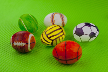 Chicken egg with a pattern under sports balls, on the green background.