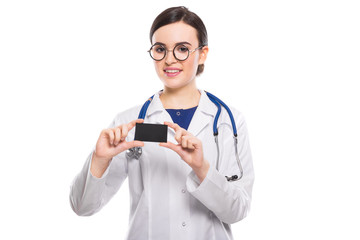 Successful young woman doctor with stethoscope showing business card in white uniform on white background