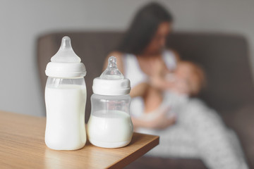 Bottles with breast milk on the background of mother holding in her hands and breastfeeding baby....