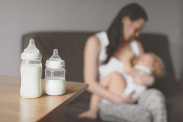 Bottles with breast milk on the background of mother holding in her hands and breastfeeding baby. Maternity and baby care. - 193809346