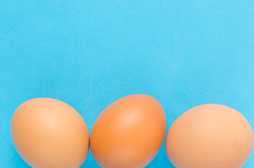 Three brown, chicken eggs blue background.