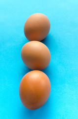 Three brown, chicken eggs blue background.