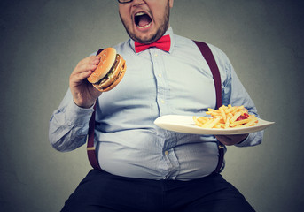 big man in formal clothes sitting and consuming plate with fast food - obrazy, fototapety, plakaty