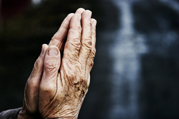 Hands of an old grandmother in prayer on a dark background