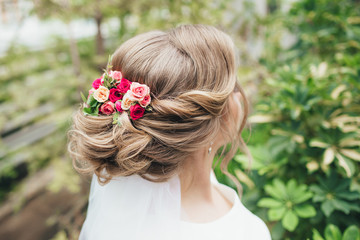 Naklejka premium Fashionable wedding hairstyle with fresh roses. Beautiful styling, rear view. The bride stands with his back to the camera.
