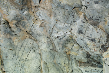 Natural stone grunge grey-brown uneven wall with cracks.