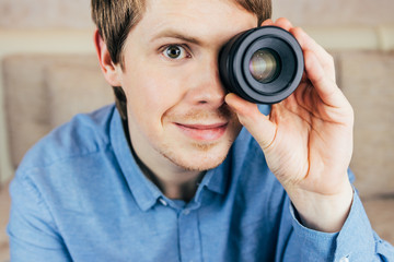 Young male photographer holds camera lens in his eye. Close-up