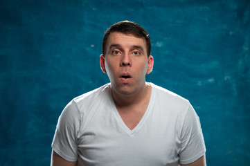 Shocked man wearing white t-shirt posing on blue background