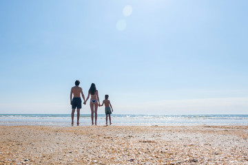 Unrecognizable family standing on the beach and looking at sea Mom son and dad hold hands back view.