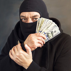 Thief in balaclava with dollars in hand. Corruption. Bribe. Fraud.
