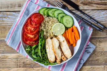 Healthy salad bowl with quinoa, tomatoes, chicken, cucumber, lime and arugula