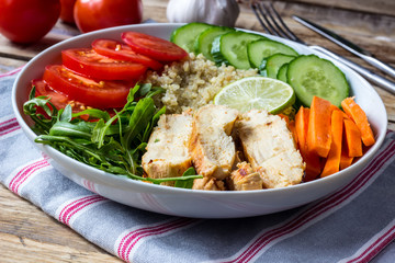 Healthy salad bowl with quinoa, tomatoes, chicken, cucumber, lime and arugula