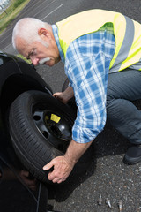 aged man changing leaking tire on the verge