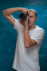 Obraz premium Smiling middle-aged man in white shirt with camera in his hands posing on blue background.