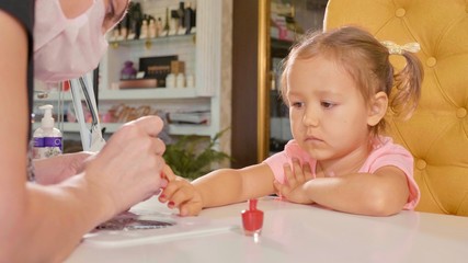 Beautician applying nail polish to kid's nail in a nail salon.