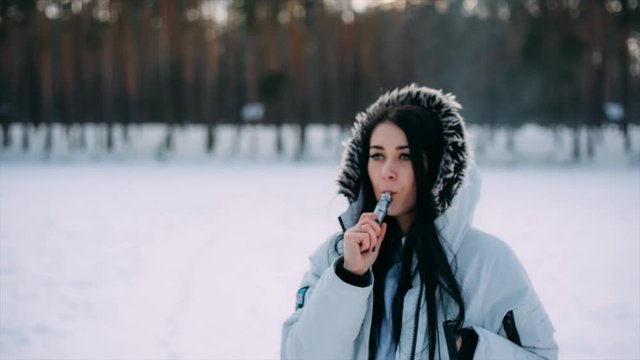 Pretty young girl vaping outside in good sunny winter weather.