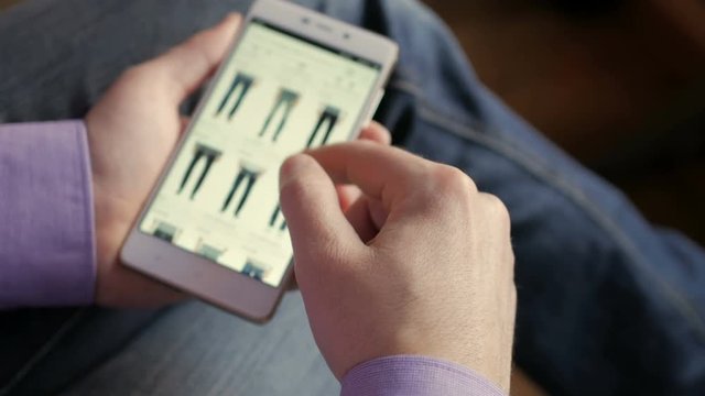 A man looks at the goods in the online clothing store. People using Smartphone, online shopping.  The screen is blurred.  Close-up. 4K UHD.