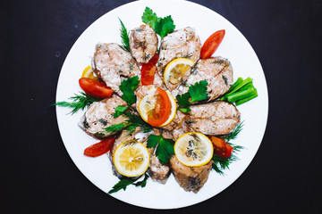 Baked salmon fish fillet with tomatoes, spices., lemon on a white plate on a black background. Diet menu.