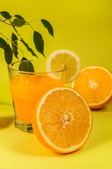Orange juice in a glass beaker and citrus slices on a yellow background with copy space