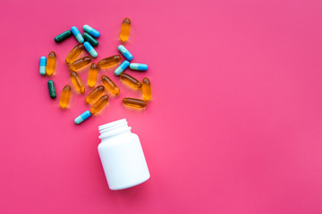 Color blue and yellow pills spilling out of a pill bottle on pink background top view copy space