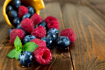 Berries of Blueberries and Raspberries, Poured from Basket, with Drops Water on Wooden Background.