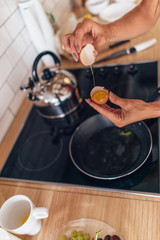Fit woman in kitchen cracking egg into frying pan