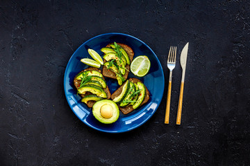 Snacks with avocado. Avocado toast with rye bread on black background top view copy space