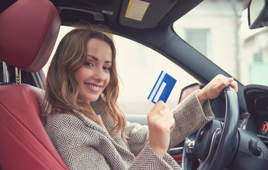 Happy woman sitting inside her new car showing credit card