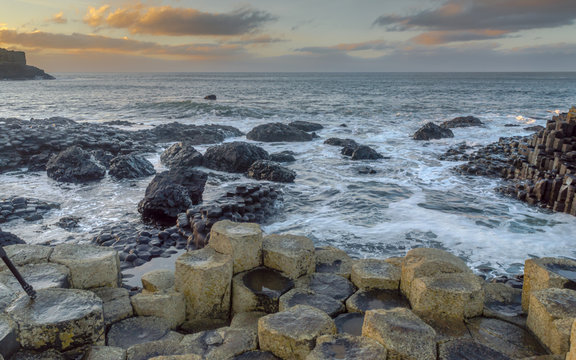 Giant's Causeway, North Ireland, UK during winters. The fierce waves batter the iconic coastline of North Ireland. In a distance the sky is lit with sun rays just before sunset.