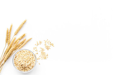 Cereals concept. Oatmeal in bowl near sprigs of wheat on white background top view copy space