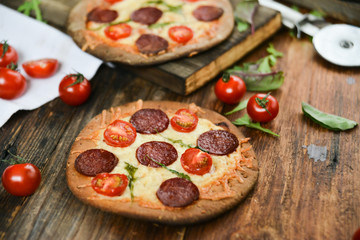 Mini Pizza With Cherry Tomatoes And Salami Sausages On A Wooden Background Natural Rustic, A Pizza Cutter And Ingridienty.