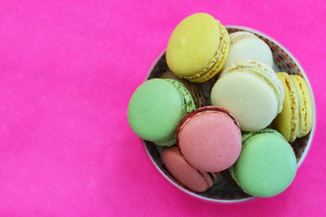 Obraz na płótnie Canvas Colorful macaroons in bowl on vivid pink surface with copy space 