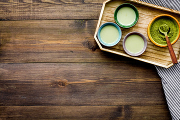 Fototapeta na wymiar Japanise tea ceremony with matcha tea. Bowl with powder and cups with beverage on tablecloth on dark wooden background top view copy space
