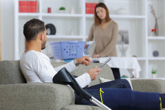 Woman ironing, man on sofa with leg injury