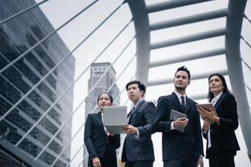 Fototapeta premium Group of business peoples standing outdoors with office building in the background, look to target at the sky