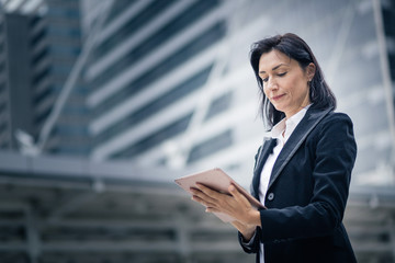 Caucasian businesswoman with wireless tablet standing outdoors with office building in the background, low angle view