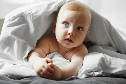 Cute baby with bewildered look sits on spacious bed