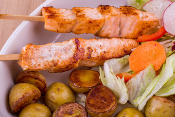 Fillet of a salmon on wooden brochettes with fried pass potatoes and lettuce leaves
